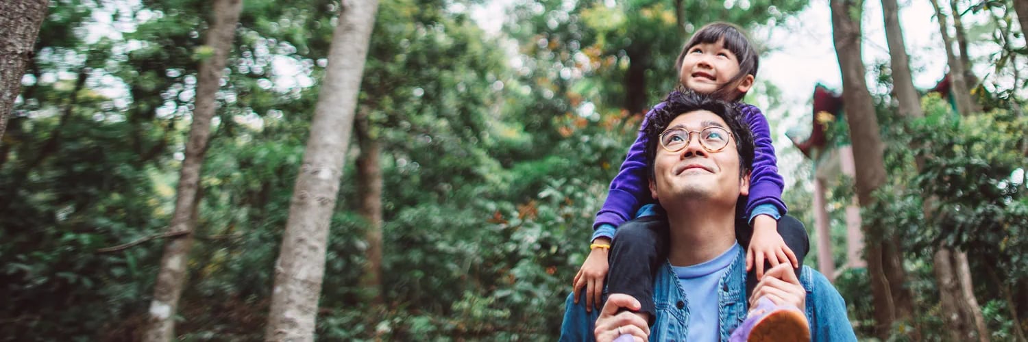 child on man's shoulder's in a forest