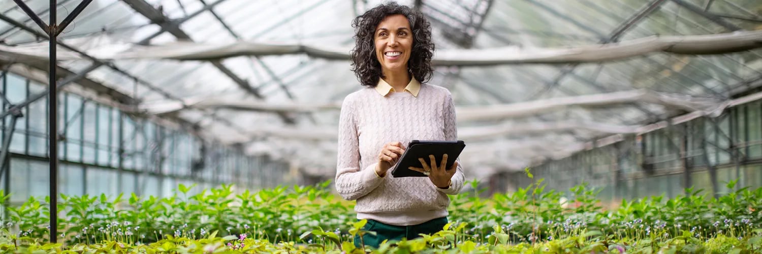 woman smiling holding a tablet while in a greenhouse