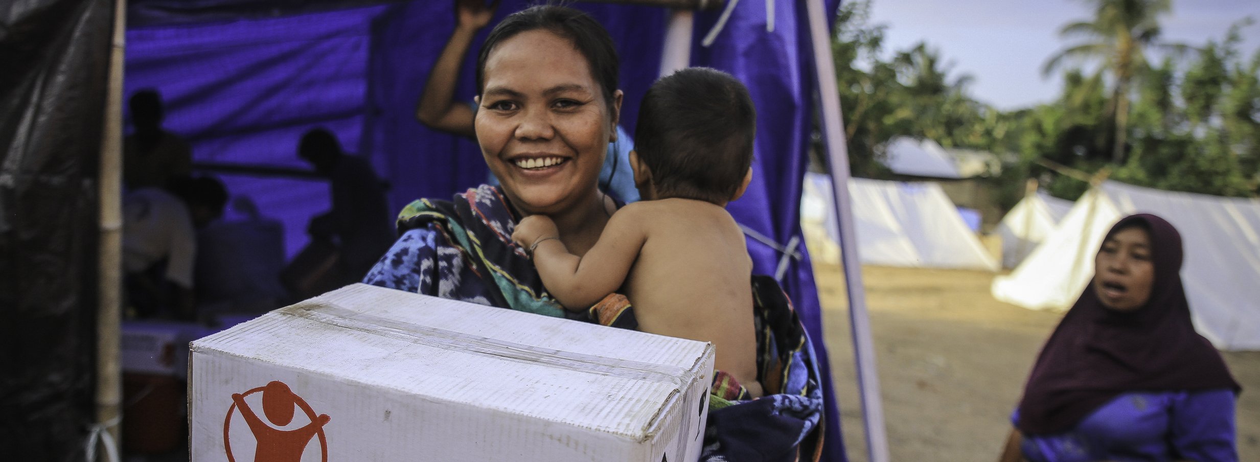 woman carrying her child and a box of disaster relief package labelled Save the Children